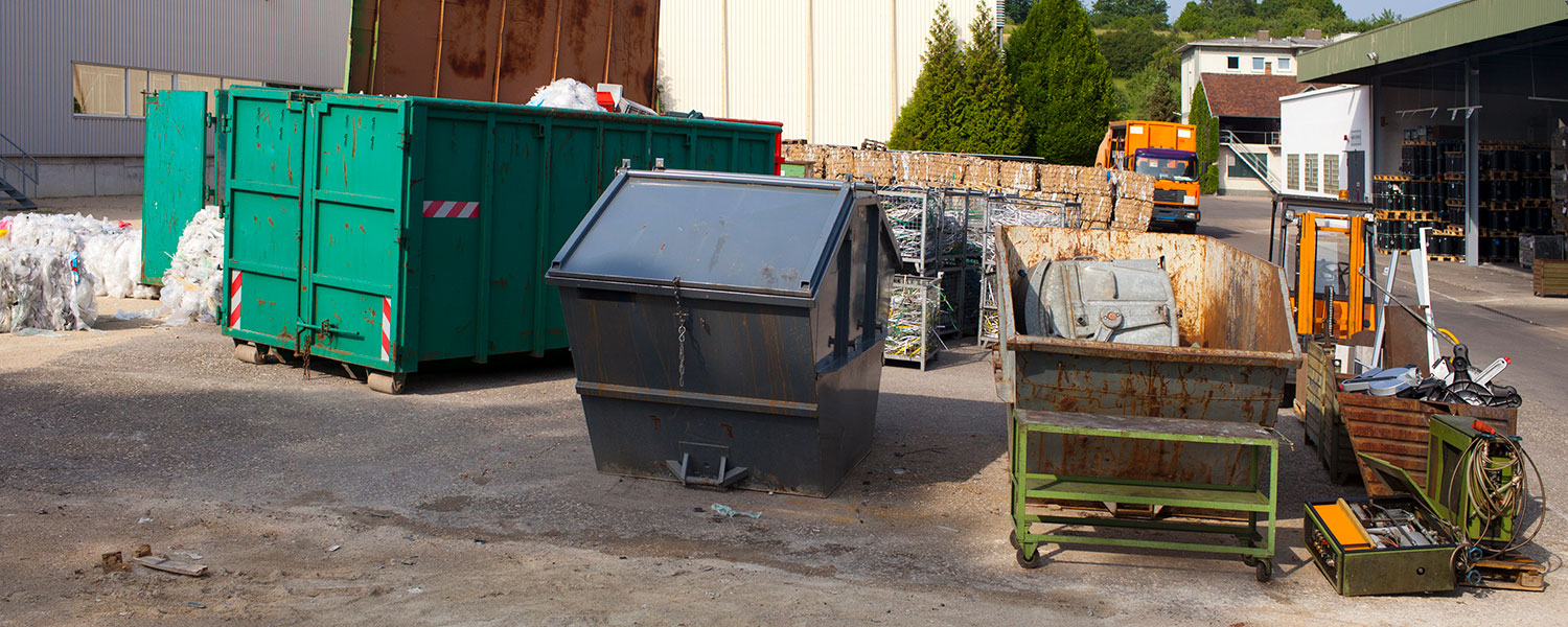 Multiple dumpsters on a job site including a construction dumpster and a small front load commercial dumpster.